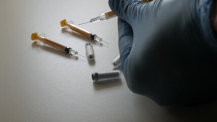 Gloved hand handling syringes on a table, calm medical scene