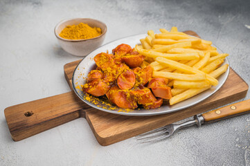 German currywurst with crispy fries on metal plate over wooden board and concrete background ideal for street food ads and stock images.