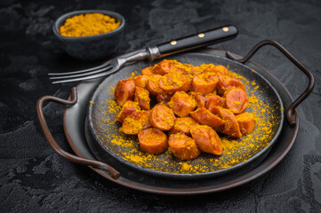 German currywurst, sausages  with curry spice served on rustic metal plate over dark textured background perfect for street food and stock imagery.