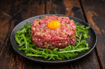 Raw beef tartare with egg yolk and arugula on wooden surface great for gourmet cooking protein rich meals and high quality food photography.