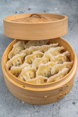 Fresh steamed jiaozi arranged in bamboo steamer with sesame seeds on gray textured surface great for culinary stock imagery.