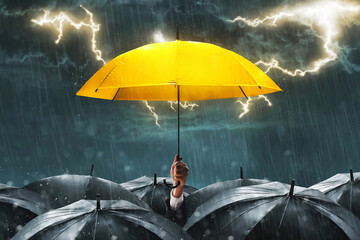 Businessman hand holding yellow umbrella in crowd, heavy rain dark cloudy storm