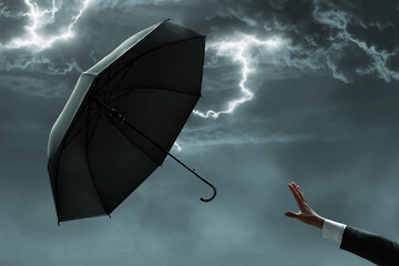 Businessman hand catching black umbrella flying in stormy sky