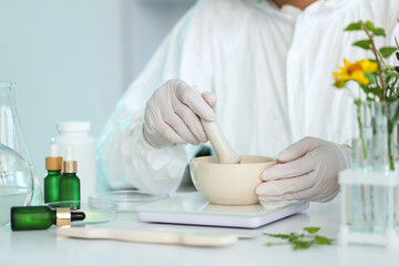 Young female biologist with mortar and pestle working in lab, closeup