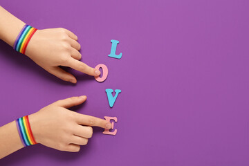 Female hands with rainbow ribbons and word LOVE on violet background. LGBT concept