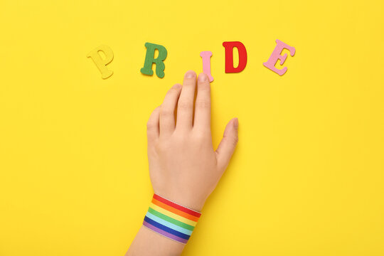 Female hand with rainbow ribbon and word PRIDE on yellow background. LGBT concept