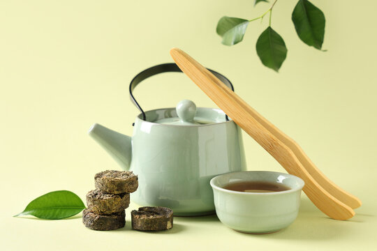 Dry pressed puer tea with cup, teapot and wooden tongs on green background