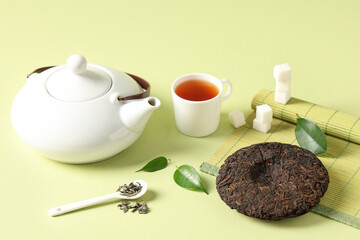 Dry pressed puer tea with teapot, cup, sugar cubes and bamboo mat on green background
