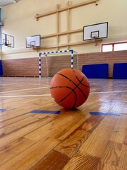 A basketball on the floor of a gymnasium with basketball hoops in the background
