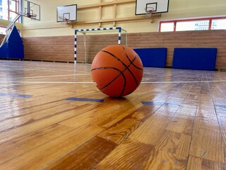 A basketball on the floor of a gymnasium with basketball hoops in the background
