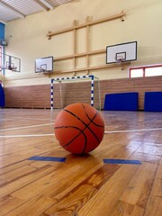A basketball on the floor of a gymnasium with basketball hoops in the background
