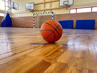 A basketball on the floor of a gymnasium with basketball hoops in the background
