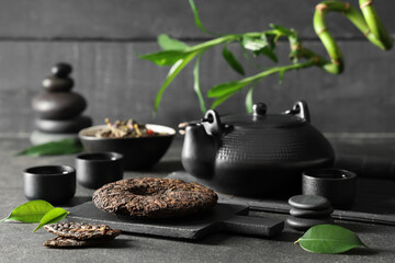Dry pressed puer tea with teapot, cups and stones on grey grunge table against wooden wall
