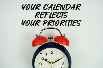 Your Calendar Reflects Your Priorities text with alarm clock flat lay on white background