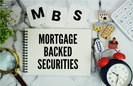 MBS Mortgage-Backed Securities text written on notepad with house model, calculator, magnifying glass and alarm clock on marble background