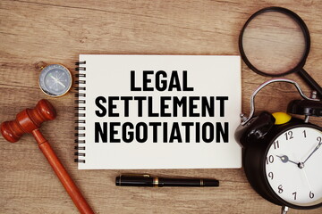 Legal Settlement Negotiation message written on notepad with alarm clock, wood gavel and magnifying glass flat lay on wooden background
