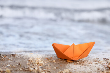 Orange paper boat on shore near water, closeup
