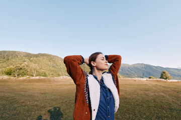 Fototapeta premium Woman in autumn jacket stands in meadow with mountains in background, portrait of relaxation and outdoor lifestyle, enjoying fresh air and scenic nature landscape.
