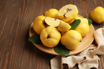 Plate with sweet ripe quinces and leaves on wooden background, closeup