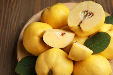 Plate with sweet ripe quinces and leaves on wooden background, closeup