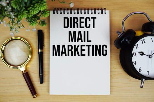 Direct Mail Marketing text written on notepad with alarm clock and magnifying glass flat lay on wooden background