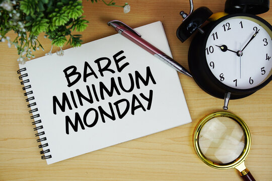 Bare Minimum Monday text written on notepad with alarm clock and magnifying glass flat lay on wooden background
