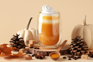 Glass of orange pumpkin spice latte and ingredients on beige background, closeup