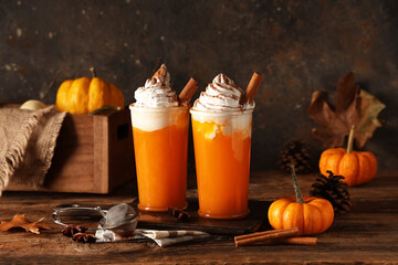 Glasses of orange pumpkin spice latte and ingredients on wooden table