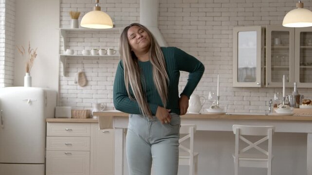 Portrait of displeased chubby black woman dressing up,, struggling to fit into small jeans after gaining weight, expressing frustration and irritation while standing in domestic room.