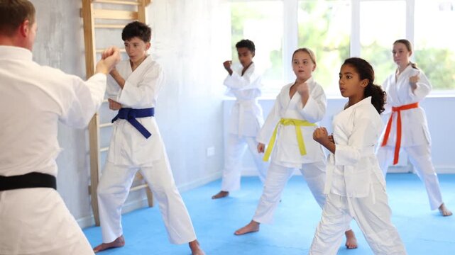  Group of boys and girls in kimonos train karate techniques in studio