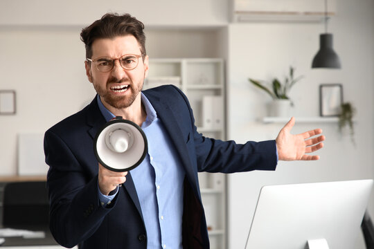 Angry businessman shouting into megaphone in office
