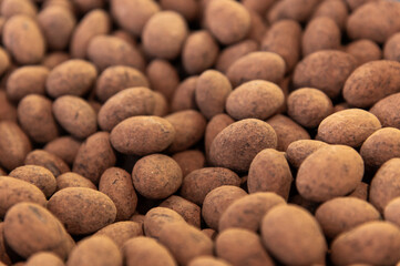 Chocolate-coated nuts in cocoa powder as a background. A profusion of nuts in a matte dark chocolate shell