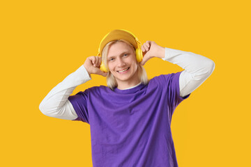 Fototapeta premium Young blonde man in hat with headphones on yellow background