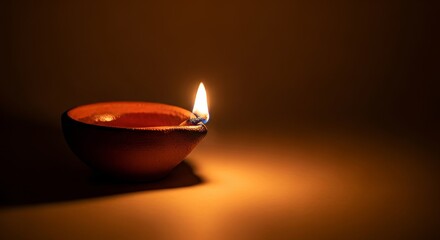 A lit diya sits on a brown surface casting a warm glow The diya is a small clay bowl holding oil and a wick that is burning brightly