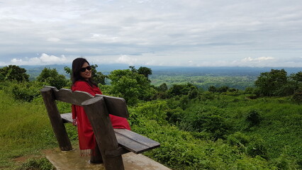 Woman sitting on a bench, looking out at the vast green landscape with a cloudy sky in the...