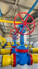 The photo shows yellow and blue gas pipes with a large red valve that shuts off the gas flow in the pipes supplying gas to homes.
