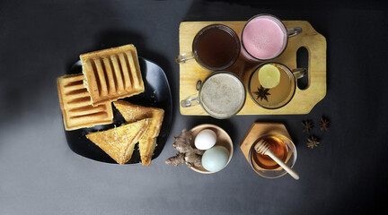 an assortment of hot drinks and snacks from indonesian cafe. pancong, toast, tea, milk, ginger, honey, egg, etc on black background