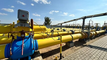 The photo shows yellow and blue gas pipes with black stripes that enter the ground from above. Gas is supplied through the pipes under high pressure.