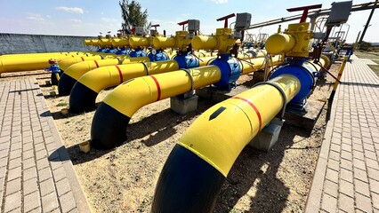 The photo shows yellow and blue gas pipes with black stripes that enter the ground from above. Gas is supplied through the pipes under high pressure.