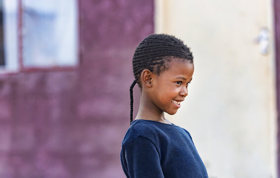 Village African child girl with dreadlocks and ponytail in front of the house, at sunset, standing in the yard