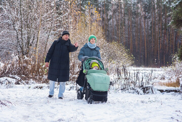  family is walking in a winter park, a teenage boy is pushing a baby stroller, his dad is walking next to him.