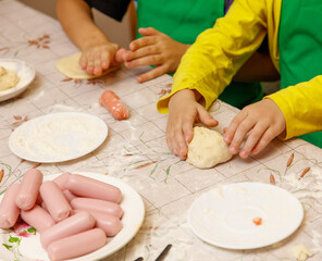 A child is making a dough with a sausage on a table