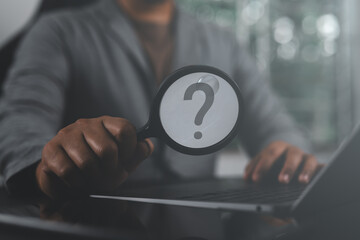 Businessman using laptop while holding a magnifying glass with question tech, Brainstorming, and problem-solving. Concept of asking, answering, and business FAQs. question mark Thinking and wondering