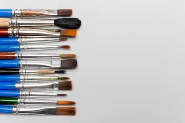 Many different brushes on a white background. Painting tools, a set of dirty paint brushes in a row on a white background, copy space, top view