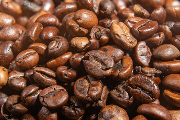 A dense layer of roasted coffee beans forms a textured carpet of browns. The tight crop focuses on surface details and flavor.