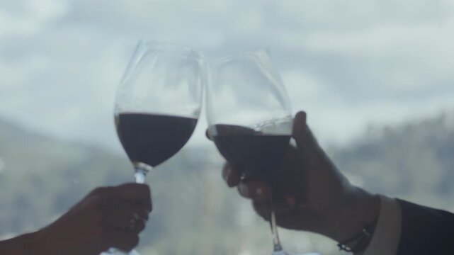 Close-up of two glasses gently clinking as they transition from initial blur to sharp focus, with a landscape visible through a window.