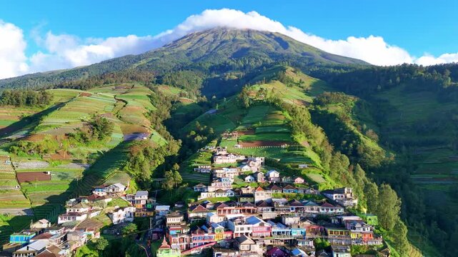 Drone footage of Nepal van Java, a vibrant mountain village in Central Java, Indonesia. The scene showcases colorful houses stacked along steep hillsides beneath Mount Sumbing&rsquo;s majestic peak.