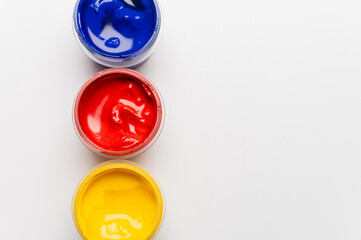 close-up shot of open small jars of gouache on a white background. A set of jars of gouache in different colors, viewed from above
