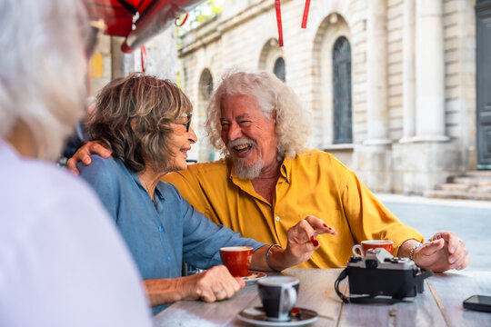Senior couple friends enjoying coffee laughing at outdoor cafe