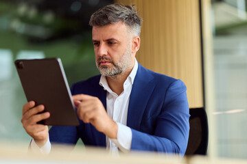 Fototapeta premium Professional Man In Blue Suit Focused On Tablet In Modern Office Setting